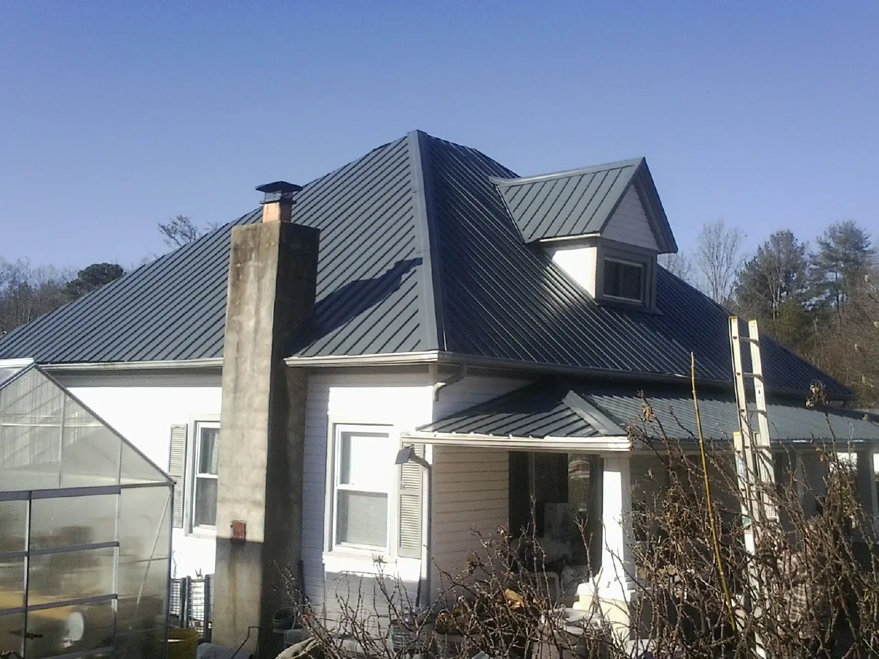 Dark blue standing seam metal roof on a white farmhouse with dormer — Slate & Tile Roof Repair by Roofing Brothers in South Hutchinson