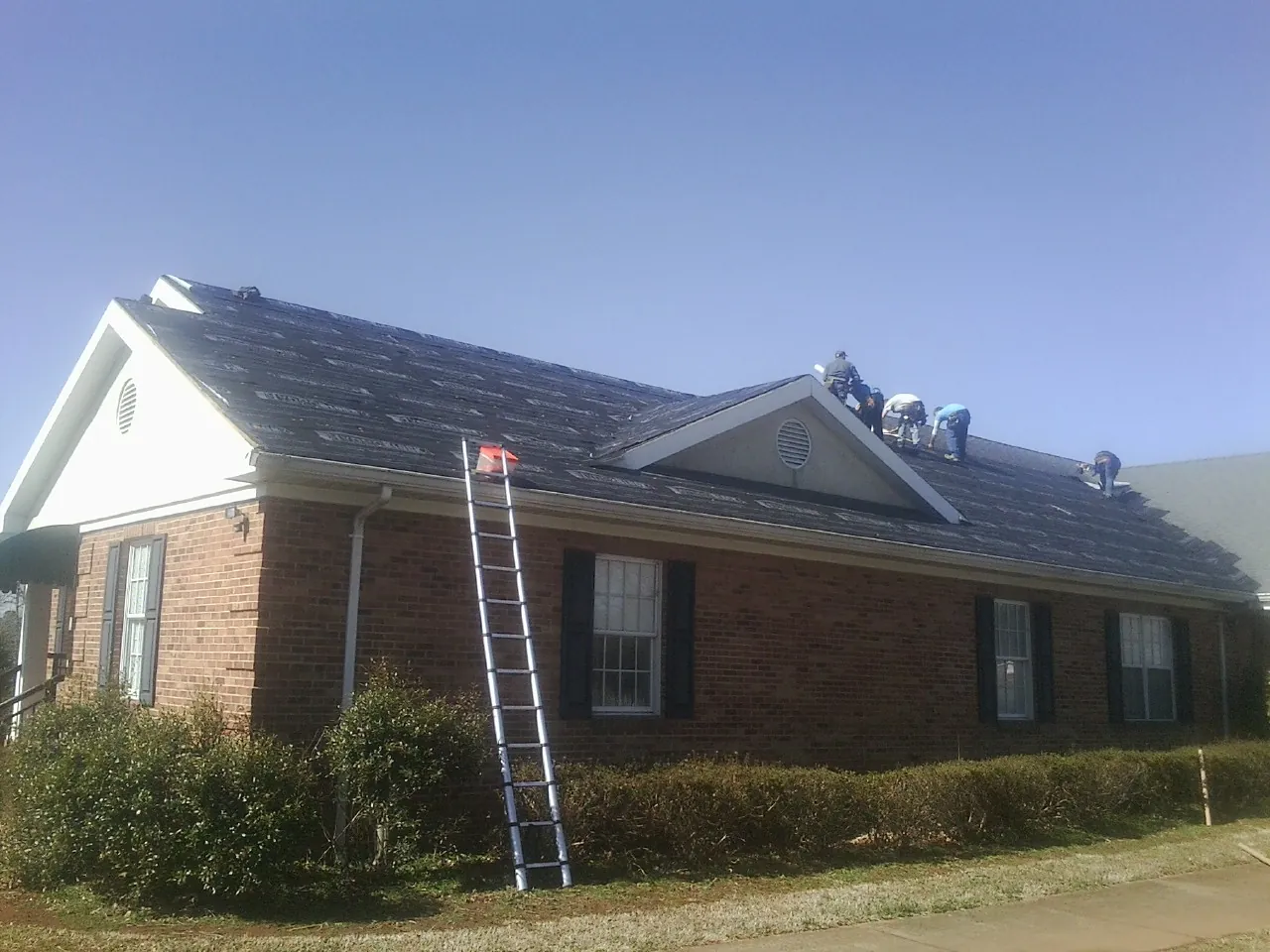 Crew tearing shingles off a brick ranch roof with a ladder set — Metal Roof Repair work by our crew in South Hutchinson
