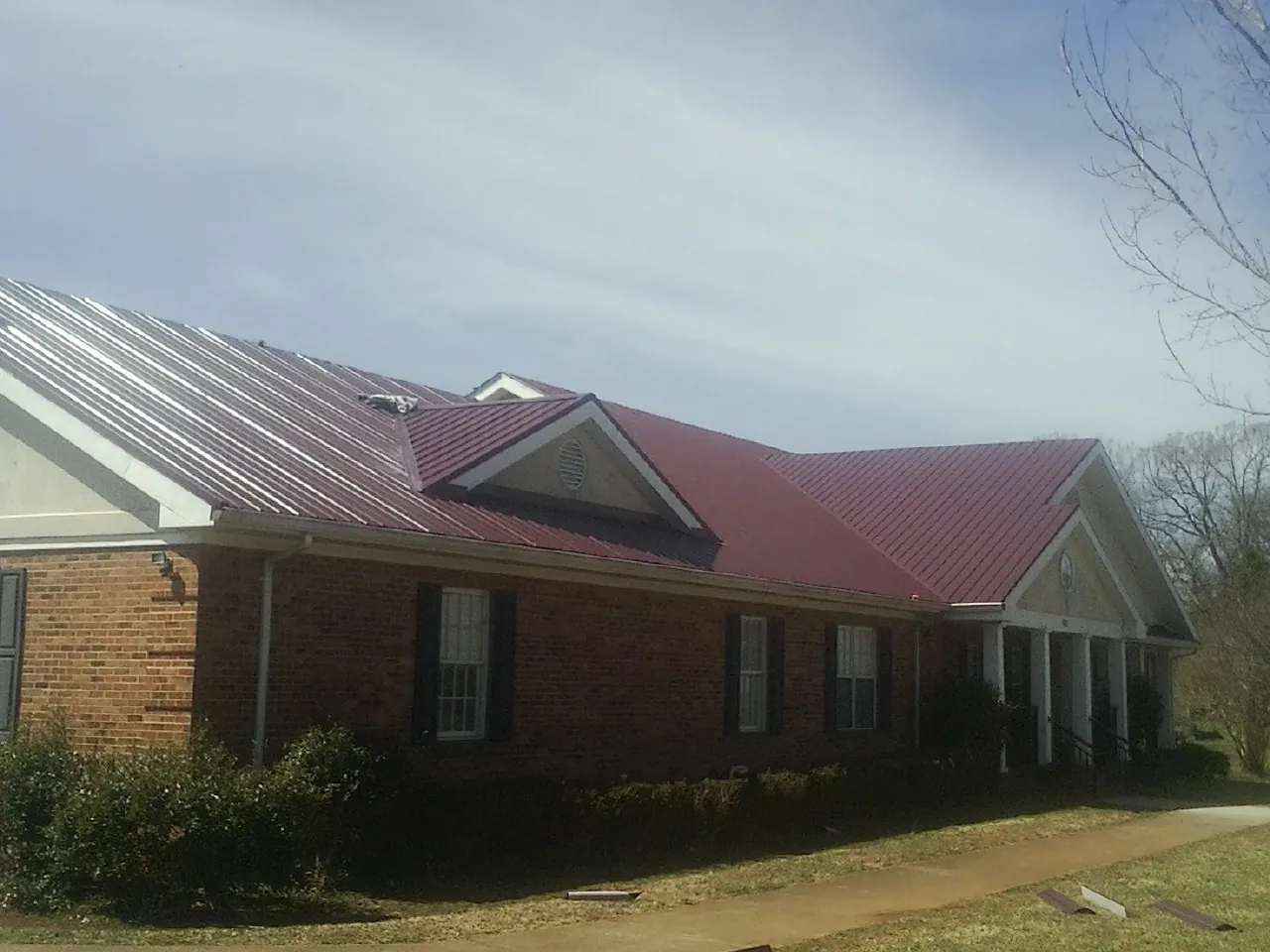 Red metal roof with gabled entries on a long brick building, from a Hail Damage Roof Repair job in South Hutchinson