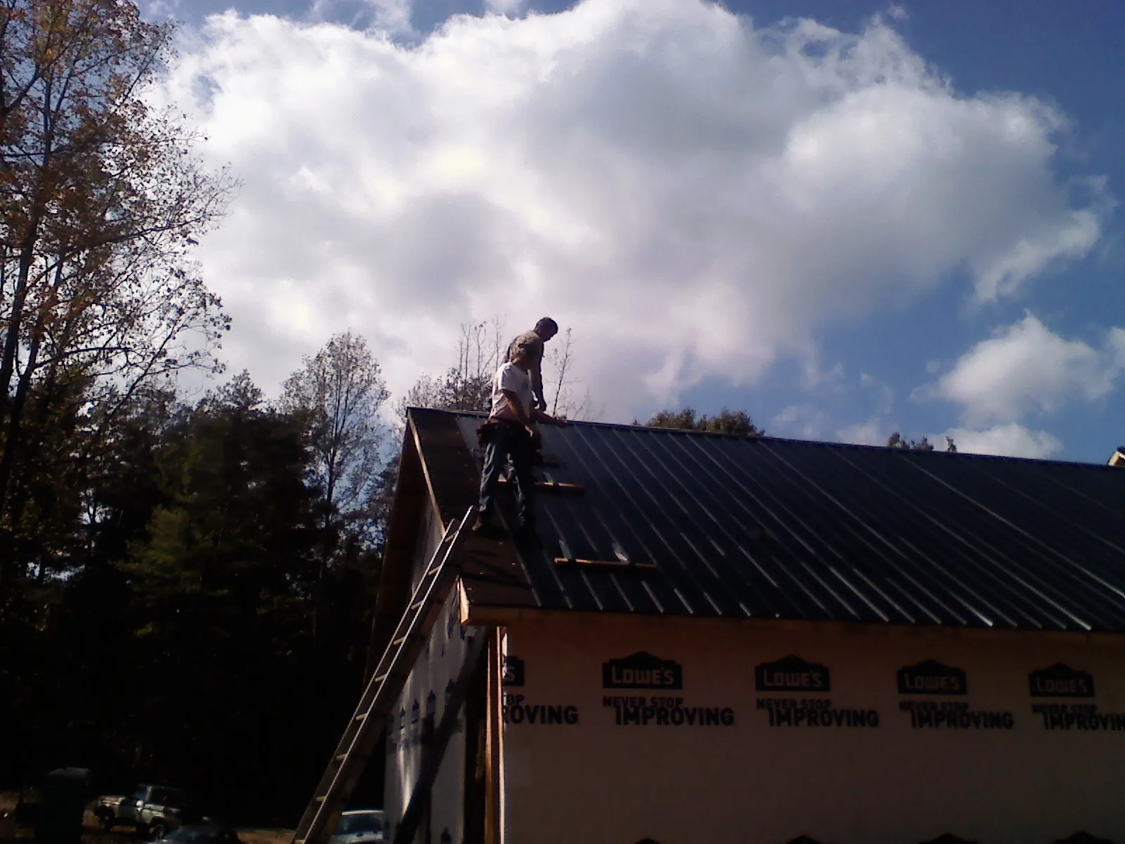 Roofer fastening dark metal panels high against a cloudy sky, from a Roof Inspection job in South Hutchinson