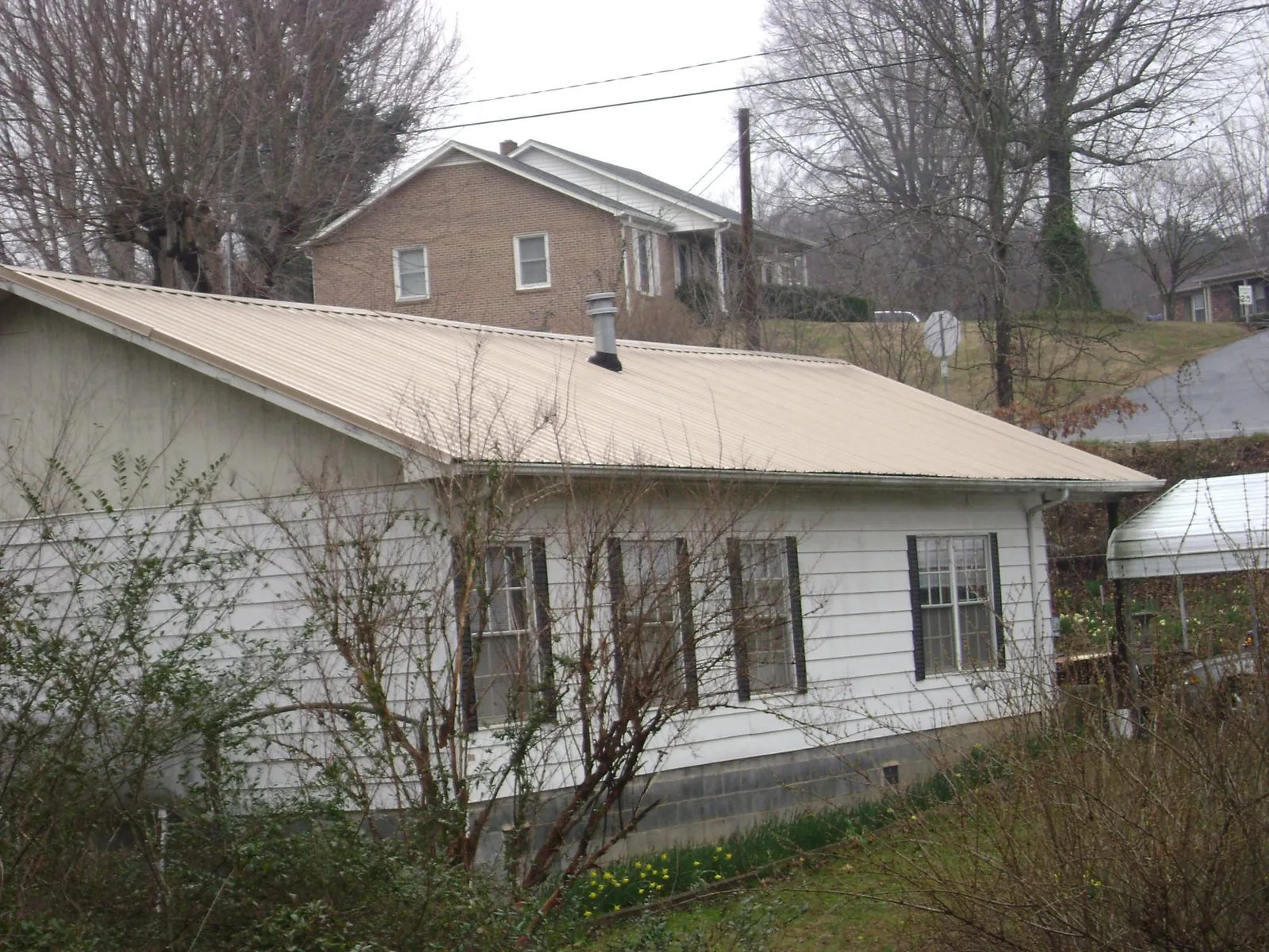 Tan metal roof on a white sided house set into a hillside — Commercial Roofing by Roofing Brothers in South Hutchinson